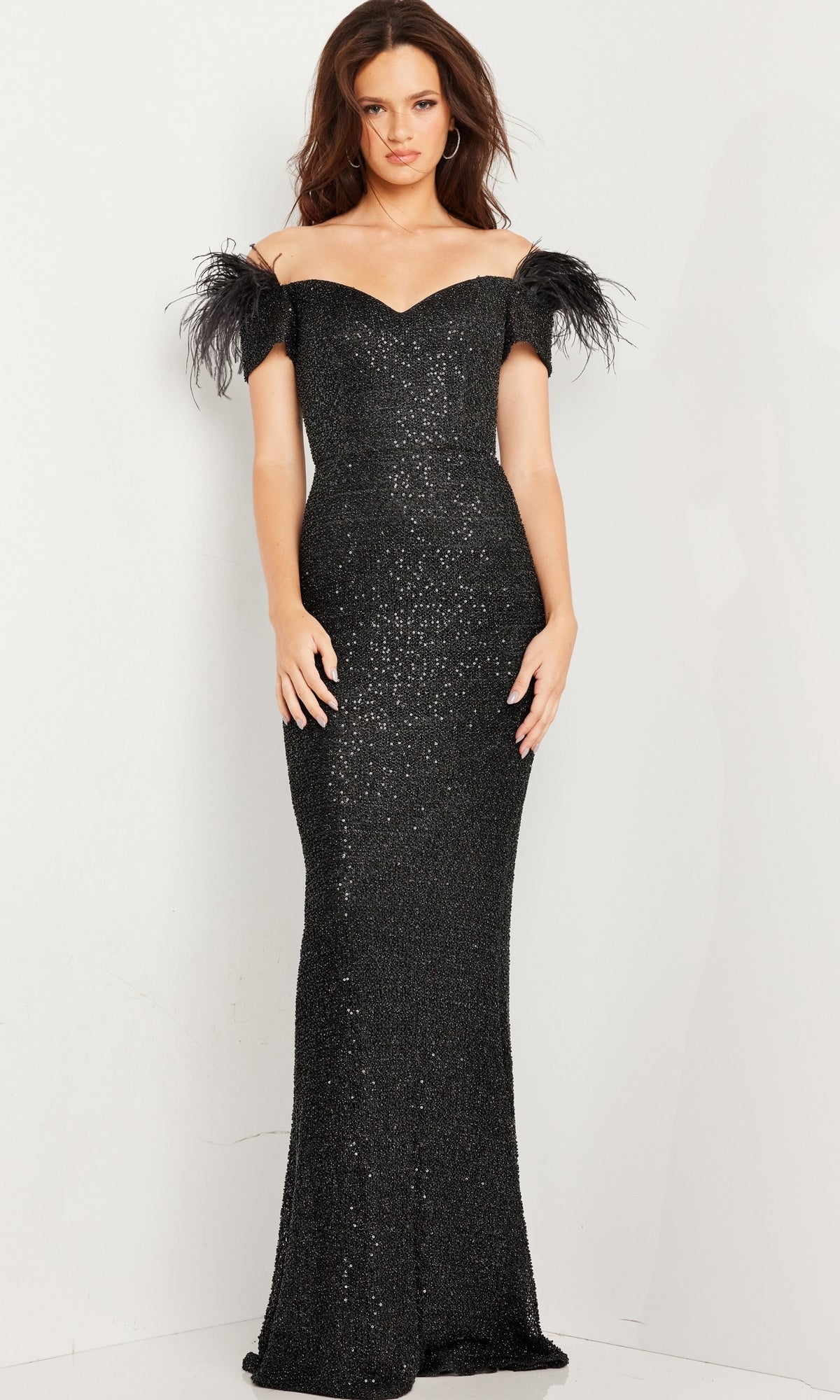 A woman stands against a plain white background wearing the Long Prom Dress 37562 by Jovani, featuring an off-the-shoulder fitted silhouette with sequin detailing and feathered sleeves.